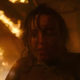 Ellie looks bloody and shaken as a building burns behind her in HBO's The Last of Us.